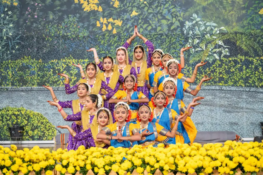 Students in classical dance costumes performing on stage, hands joined above their heads