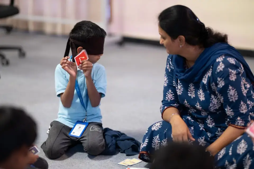 A blindfolded student identifying a card during a Brighter Minds activity with a teacher